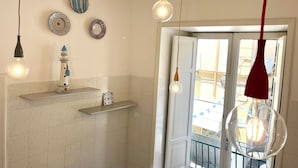 Une salle de bain avec un mur recouvert de carreaux blancs, une étagère ornée d’un objet décoratif et trois lampes suspendues.