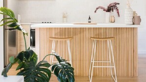 A modern kitchen with wooden cabinets, a white countertop, and two bar stools.