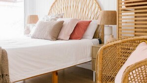 A bed with a woven headboard, a wicker chair, and a lamp on a wooden floor.