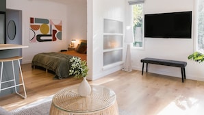 A modern living room with a bed, a TV, a bench, and a decorative plant. - The Byron - Luxury Seaside Kingston Park Studio (Kingston Park)