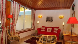 A cozy living room with a red sofa, wicker chairs, and a wooden ceiling.