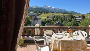 Un balcon avec une table dressée pour deux personnes, offrant une vue sur un paysage montagneux parsemé de maisons.