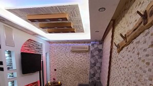 A modern living area with a stone-patterned floor, a gray sofa, a red chair, a flat-screen TV mounted on the wall, and a wooden coffee table with cups and a tray. - DESTAN KONAKLAMA (Adana)