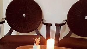 A round wooden table with a candle and a small vase on it, surrounded by dark upholstered chairs. - DESTAN KONAKLAMA (Adana)