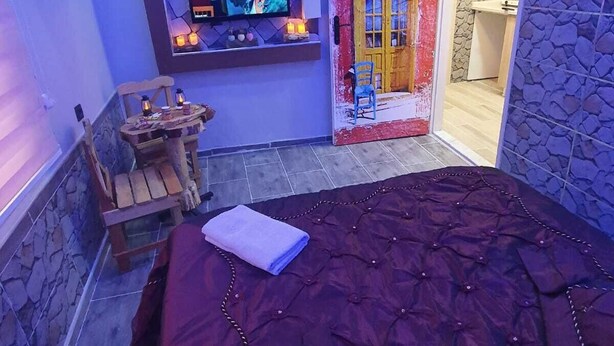 A bedroom with a large bed, a TV mounted on a wall, and a door leading to a bathroom. - DESTAN KONAKLAMA (Adana)