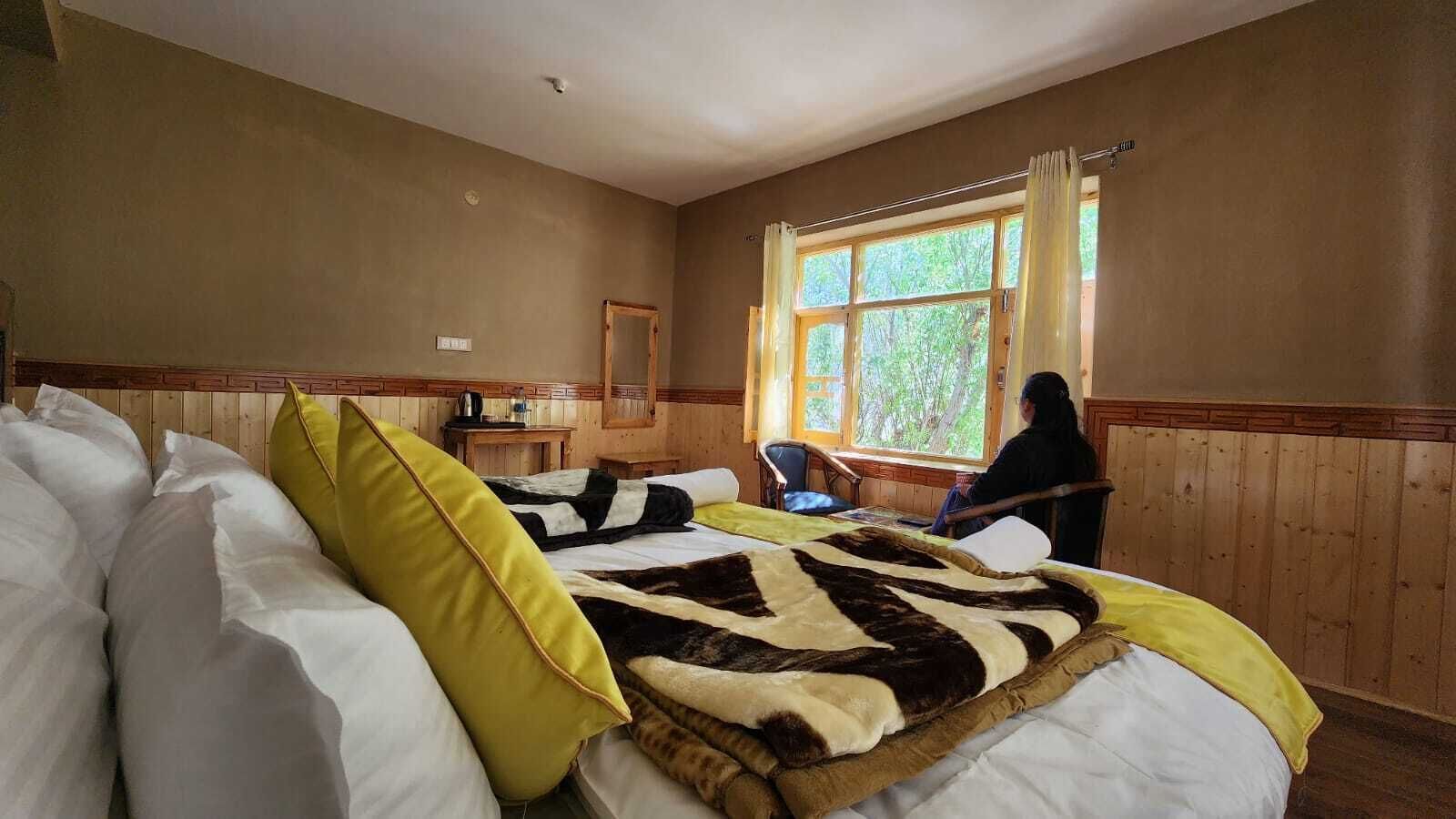 Una habitación con una cama, un escritorio de madera, una silla y un ventanal con cortinas.