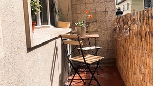 Une petite terrasse extérieure avec une table et des chaises, des plantes en pot et une clôture en bambou.
