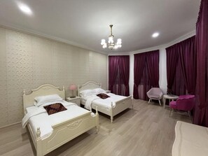 Habitación de hotel con dos camas, un candelabro, una mesita y cortinas moradas.