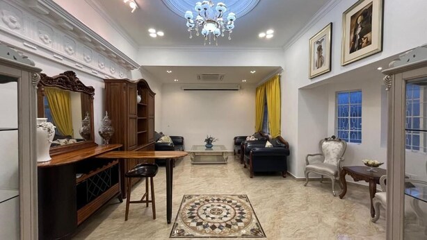 A spacious living room with a chandelier, a patterned rug, and a dining area with a wooden table and chairs.