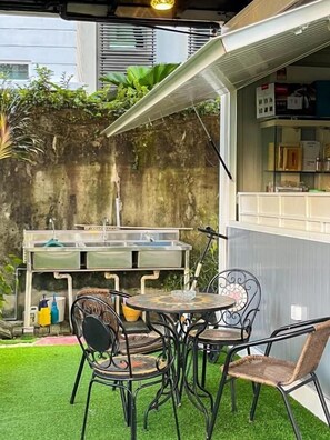 Un patio exterior con una parrilla, sillas y una mesa.