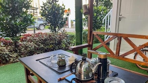A table set outdoors with a teapot, cups, and a glass on a black mat.