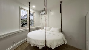 A bedroom with a four-poster bed, a window with a decorative grille, and a ceiling fan.