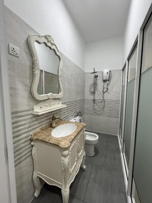 Un baño con tocador de mármol, inodoro independiente y ducha con cabezal de ducha de mano.