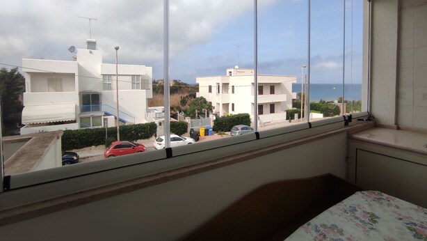 A room with a large window overlooking a residential area with modern buildings and parked cars. - Bellavista, apartment sea view with garage (Otranto)