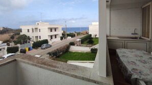 A balcony with a view of a residential street, a body of water, and a building with a white facade. - Bellavista, apartment sea view with garage (Otranto)
