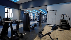 Ein modernes Fitnessstudio mit unterschiedlichen Trainingsgeräten, großen Fenstern und einer blau beleuchteten Decke.