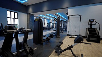 Un gimnasio moderno con varios equipos de ejercicio, amplias ventanas y techo iluminado en azul.