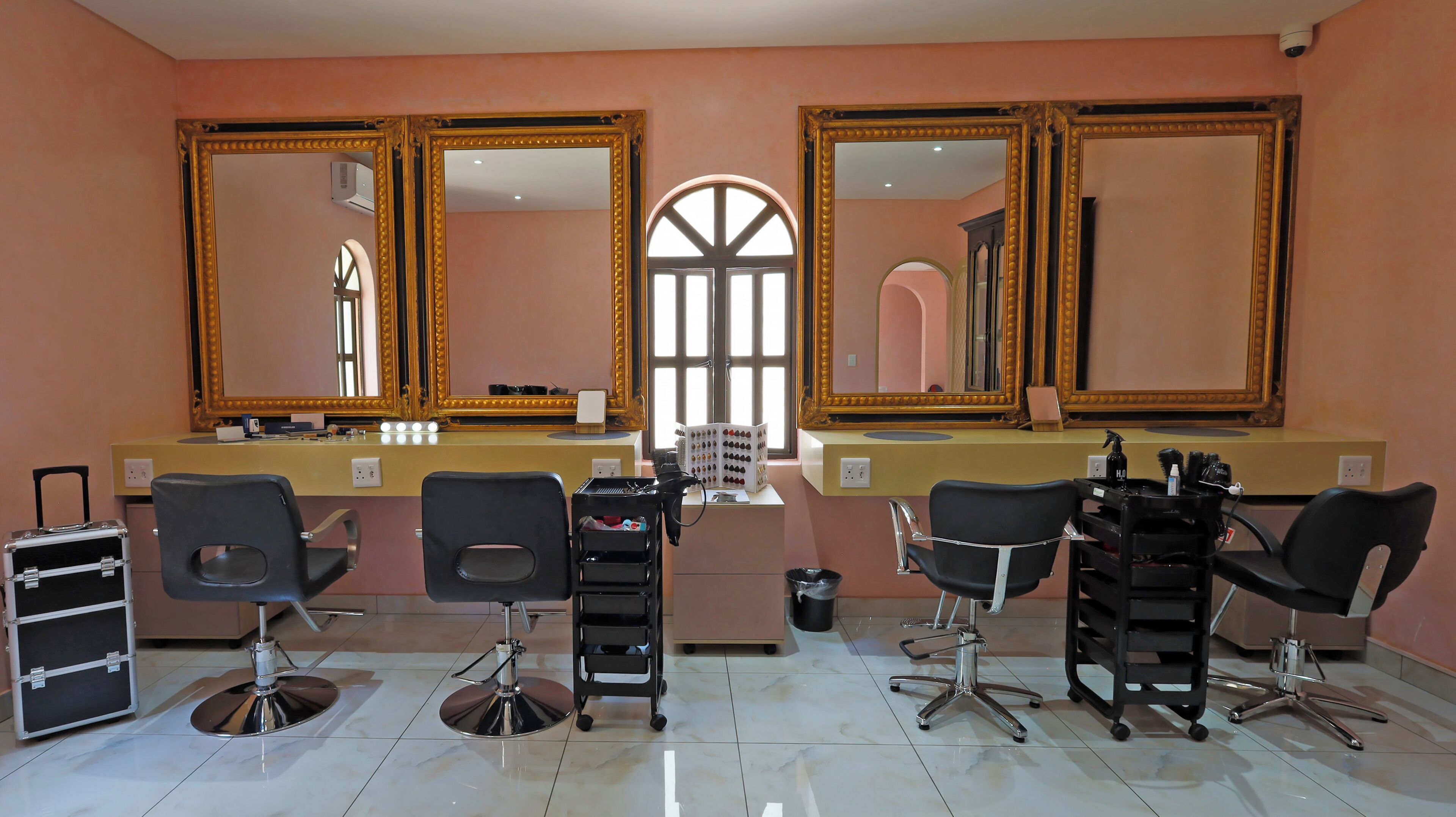 A salon with three large mirrors, a window, and multiple salon chairs.