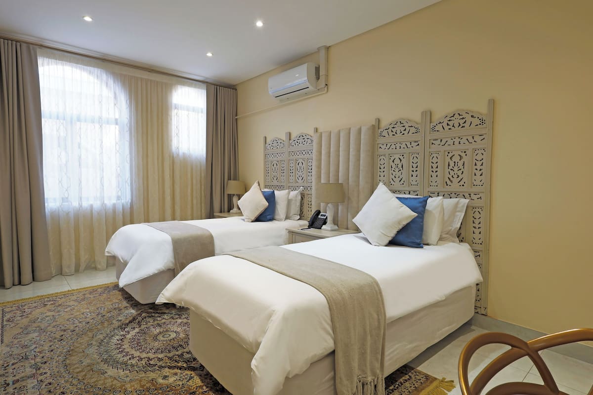 Ein Hotelzimmer mit zwei Betten, einem gemusterten Teppich, einem dekorativen Kopfteil und einer Klimaanlage.