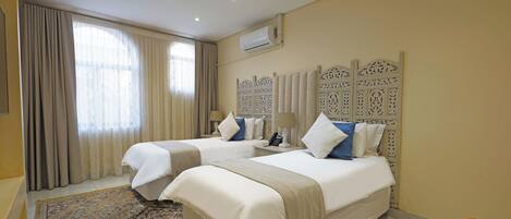 A hotel room with two beds, a patterned rug, a decorative headboard, and an air conditioning unit.