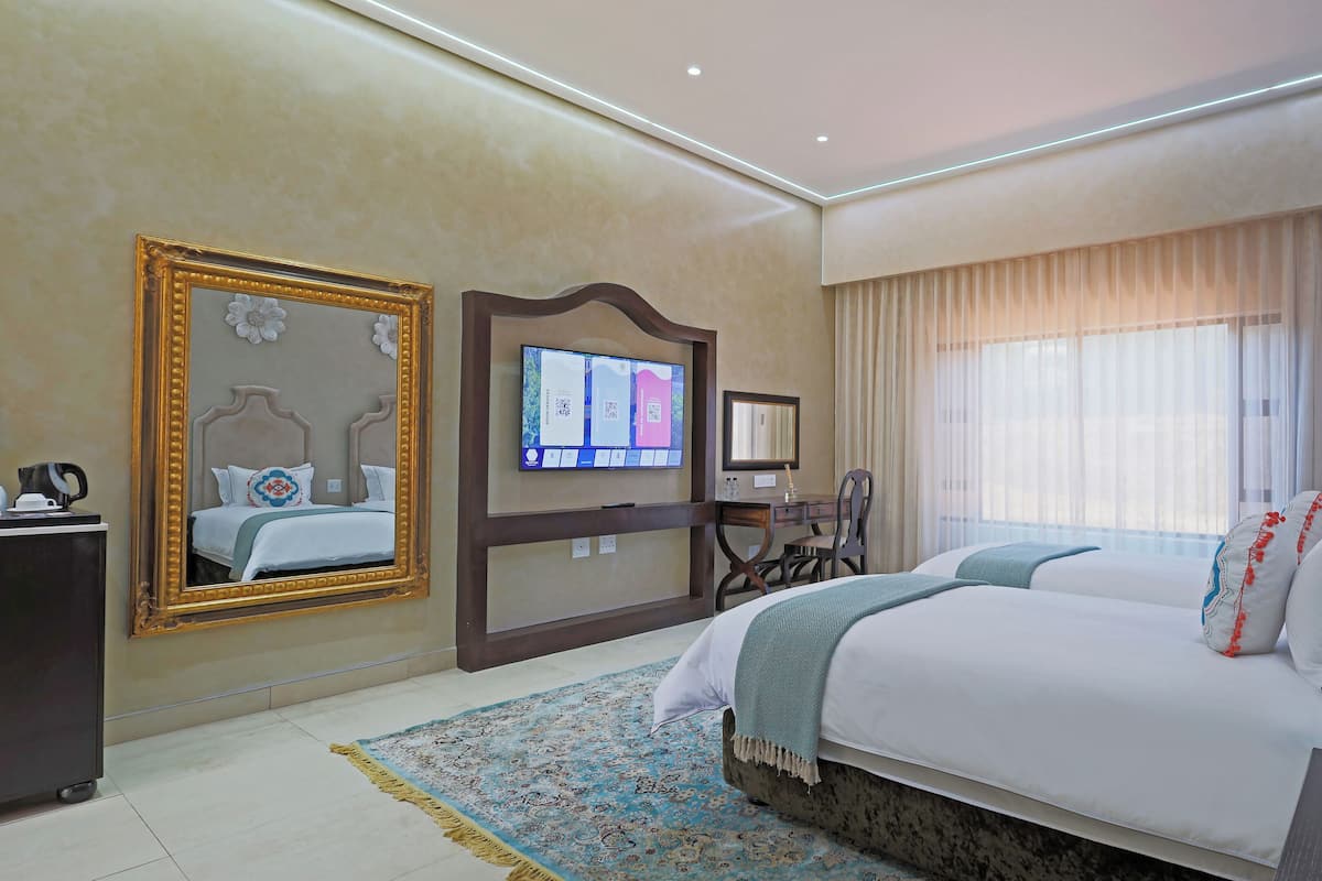 Ein Hotelzimmer mit einem großen Bett, einem Schreibtisch mit Computer, einem Spiegel und einem Fenster mit Vorhängen.