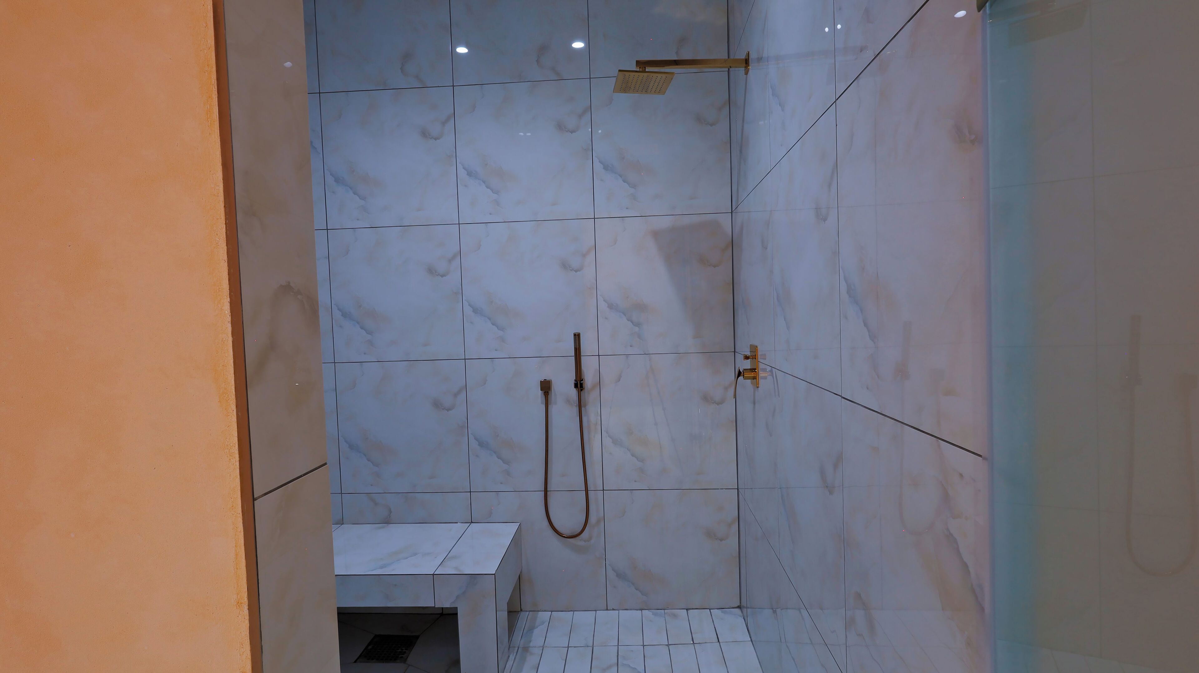 Un área de ducha con azulejos de mármol blanco y un cabezal de ducha de mano.