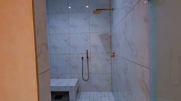 Un área de ducha con azulejos de mármol blanco y un cabezal de ducha de mano.