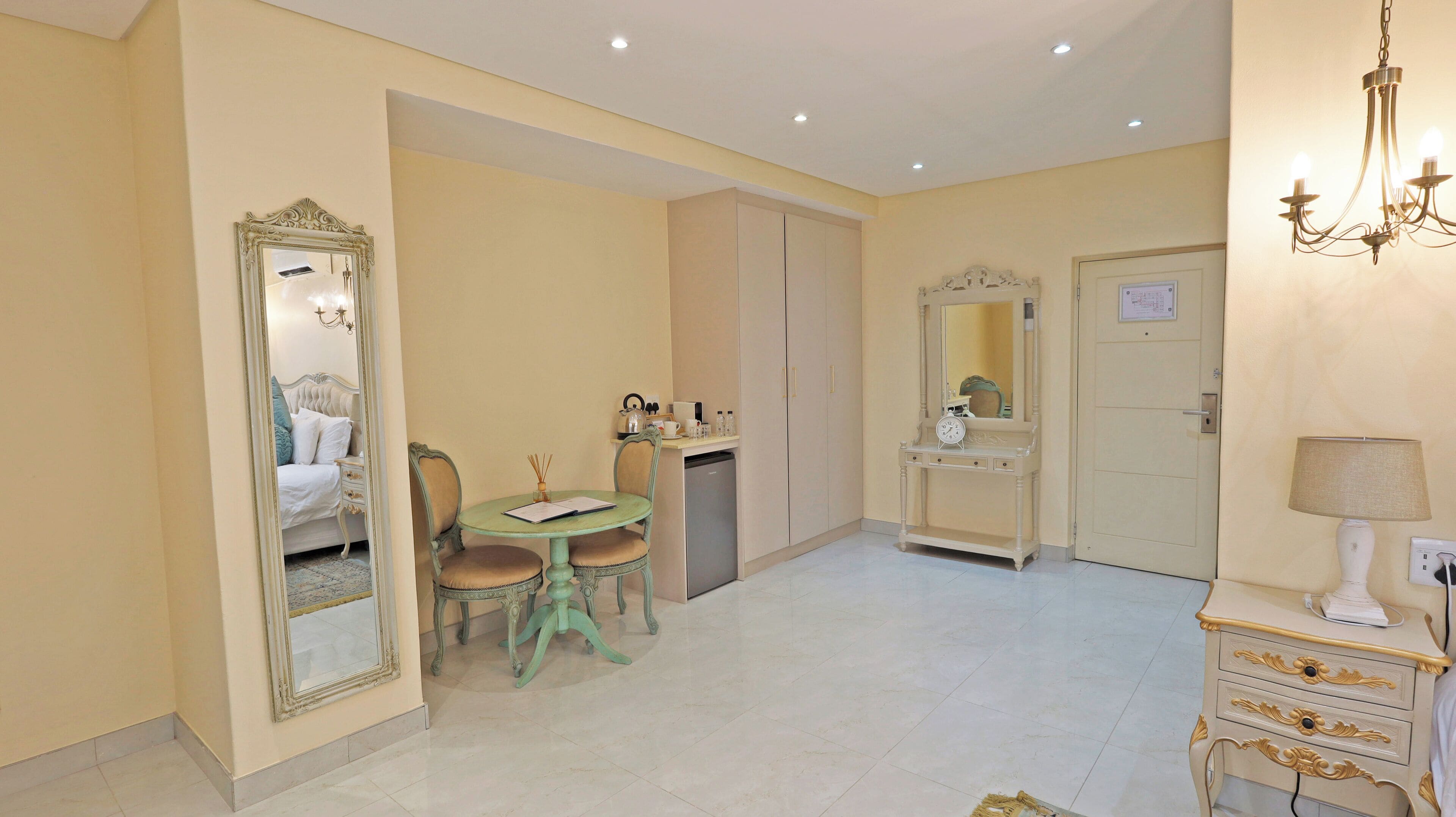 A hotel room with a bed, a vanity with a mirror, a small table with chairs, a desk with a chair, and a wardrobe.