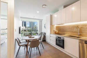 A modern kitchen with a dining area, large windows, and a view of the city. - Chic Central Apt with Gym and Pool by Zodiak Stays (Auckland)