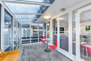 A modern interior with a glass ceiling, a seating area with red chairs, and a visible kitchen area. - Ellerslie 3BR House | Fresh Reno | Zodiak Stays (Auckland)