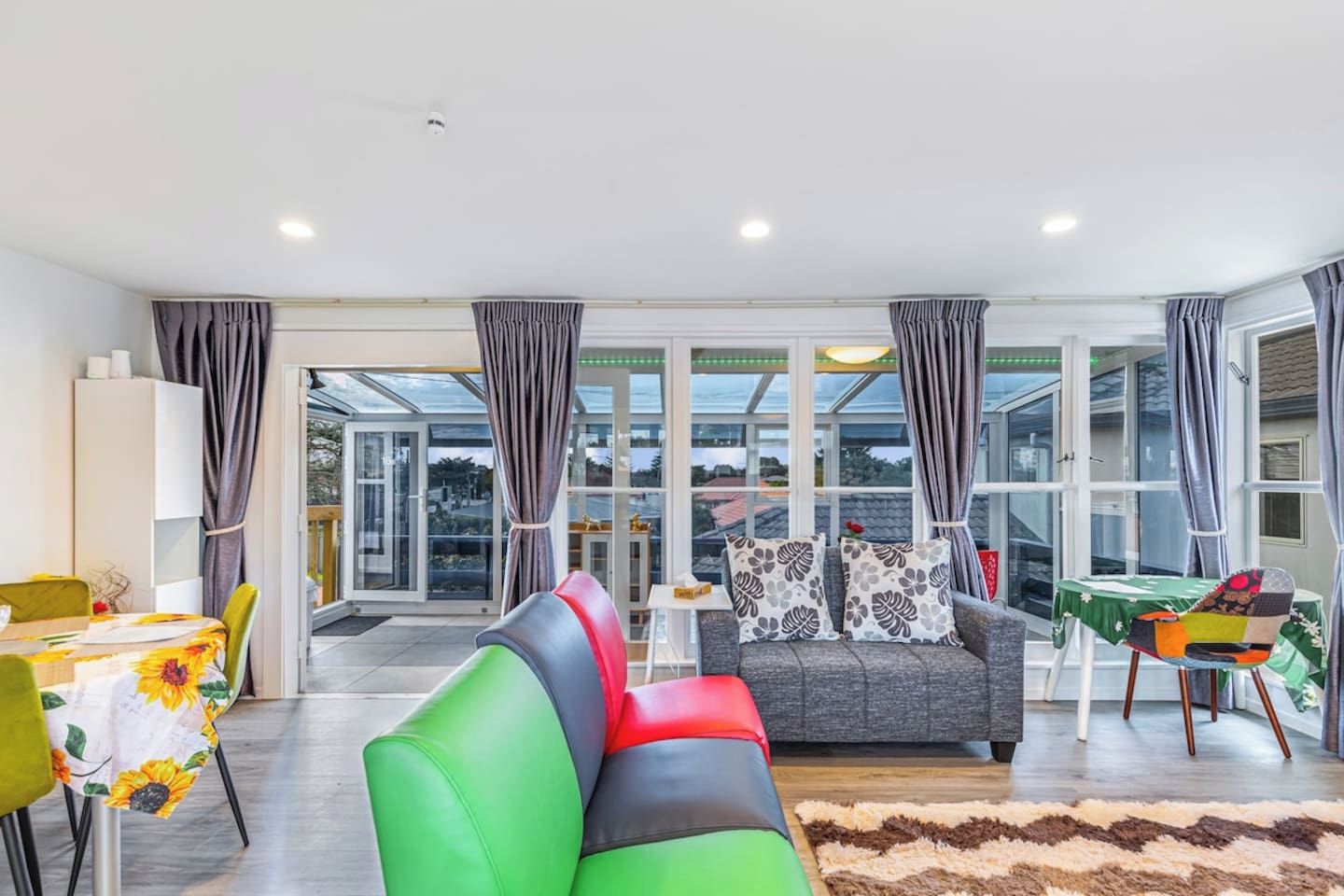 A modern living room with a sofa, a dining table, and a view through large windows.
