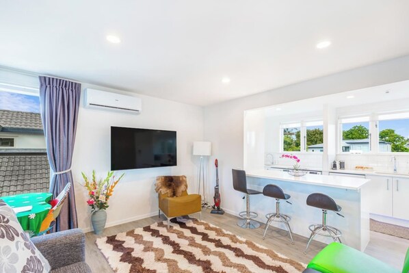 A modern living room with a flat-screen TV, a sofa, a coffee table, and a decorative rug. - Ellerslie 3BR House | Fresh Reno | Zodiak Stays (Auckland)