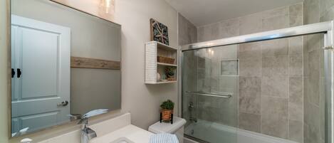 A modern bathroom with a large mirror, a sink, a toilet, and a glass-enclosed shower.