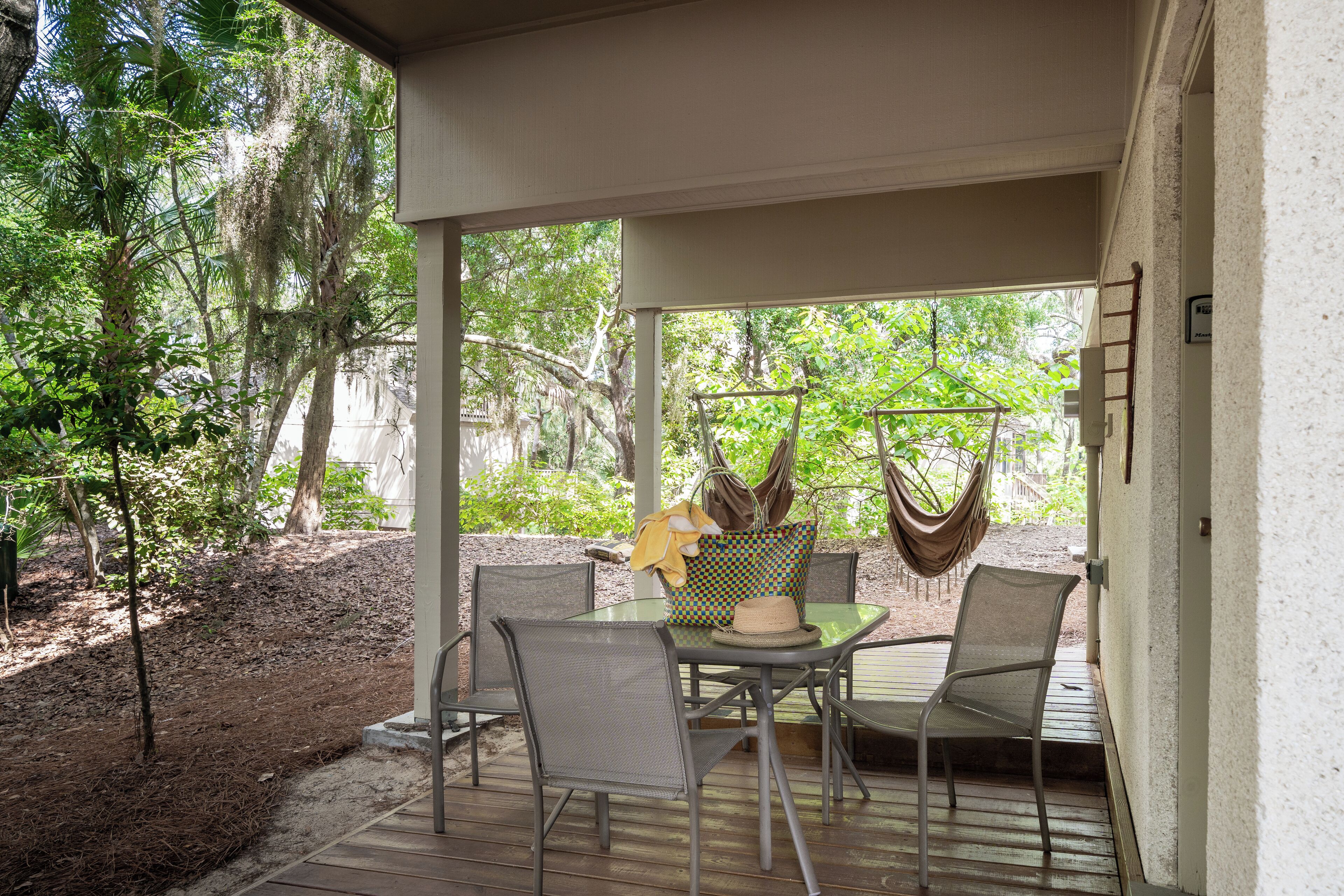 Une terrasse extérieure avec une table et des chaises, entourée d’arbres et agrémentée d’un hamac.