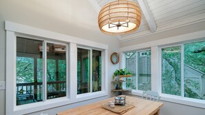 Un comedor con una mesa de madera, paredes blancas, ventanas amplias y una lámpara de techo de mimbre.