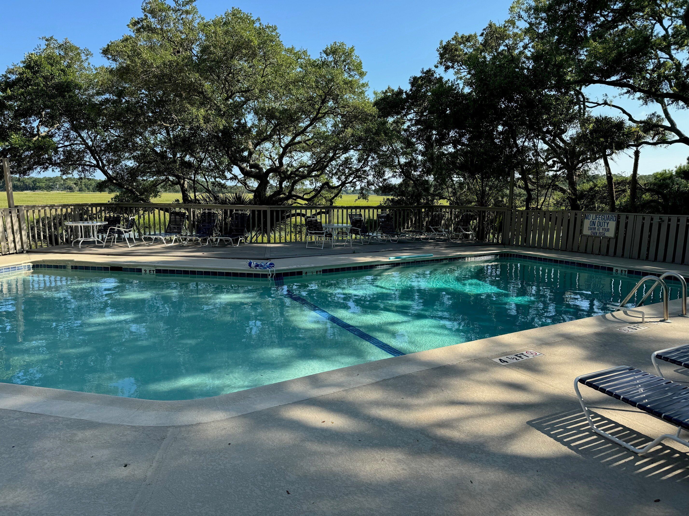 A swimming pool with lounge chairs and a wooden deck, surrounded by trees.