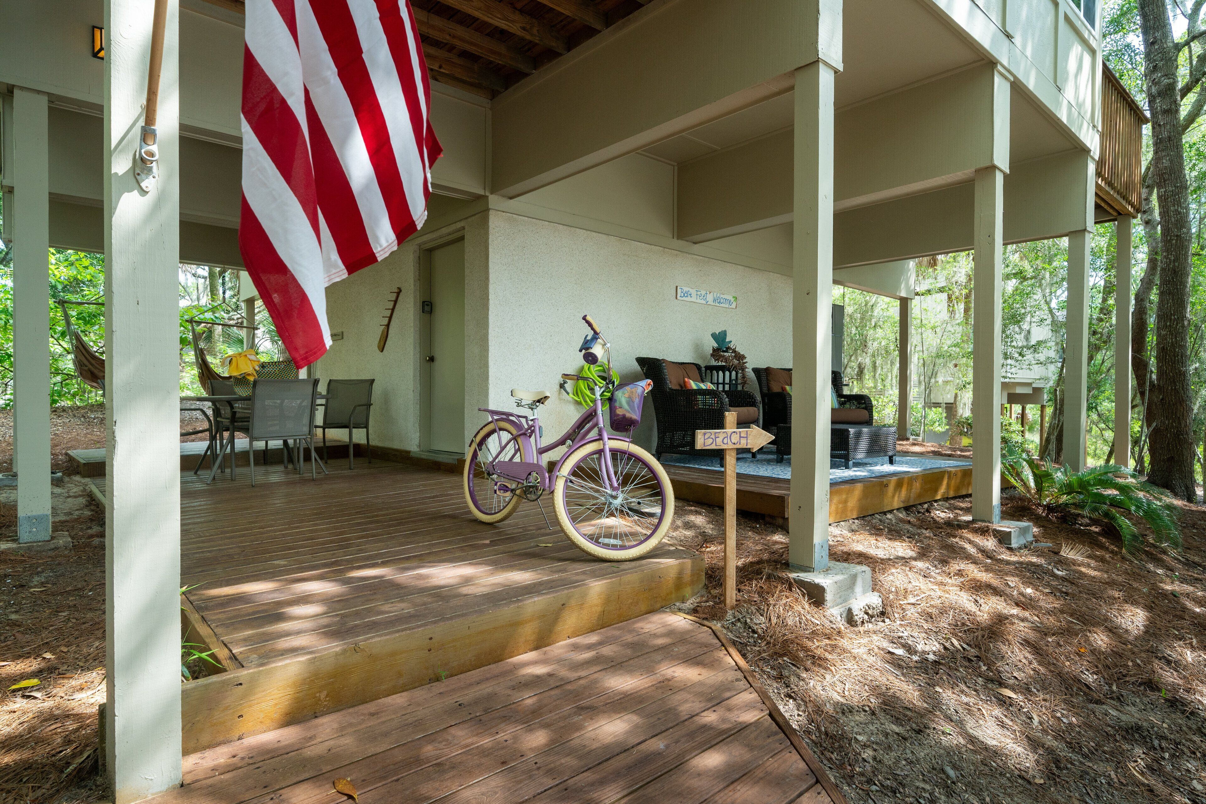 A covered porch with a bicycle, a hammock, and a sign indicating a beach direction.