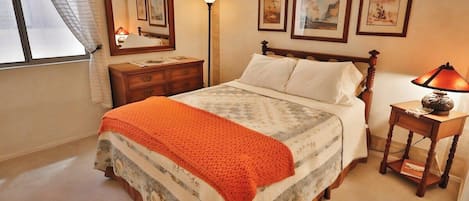 A bedroom with a bed, a nightstand, a lamp, a dresser, and framed pictures on the wall.