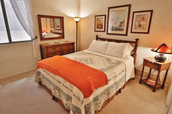 Une chambre à coucher avec un lit, une table de chevet, une lampe, une commode et des tableaux encadrés accrochés au mur.