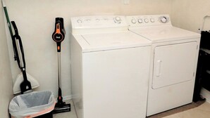 A laundry area with a front-loading washer and dryer, a broom, a dustpan, and a trash bin. - Oro Valley Vista with Sweeping Desert Views (Oro Valley)