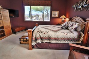 A bedroom with a four-poster bed, a wooden dresser, a television, a window with a view, and a lamp. - Oro Valley Vista with Sweeping Desert Views (Oro Valley)