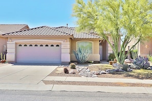 A residential house with a garage, a cactus garden, and a clear sky.