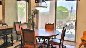 Uma sala de jantar com uma mesa redonda e cadeiras, um lustre e vista para um pátio externo através de uma porta de vidro.