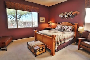 A bedroom with a large window, a wooden bed, a nightstand, a bench, and a decorative wall piece.