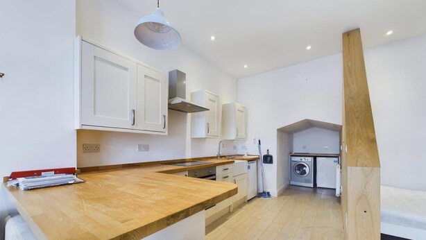 Una cocina moderna con armarios blancos, encimera de madera y lavadora incorporada.