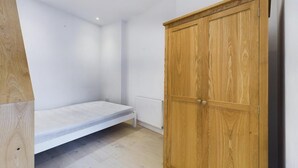 Una habitación con un armario de madera, un colchón blanco sobre el suelo y un radiador blanco.
