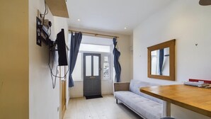 Un espacio habitable pequeño con un sofá, una mesa de madera, un cesto de basura y una puerta que da a un área exterior.