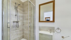 Un baño moderno con ducha envuelta en vidrio, lavamanos con argolla para toallas y un espejo en la pared.