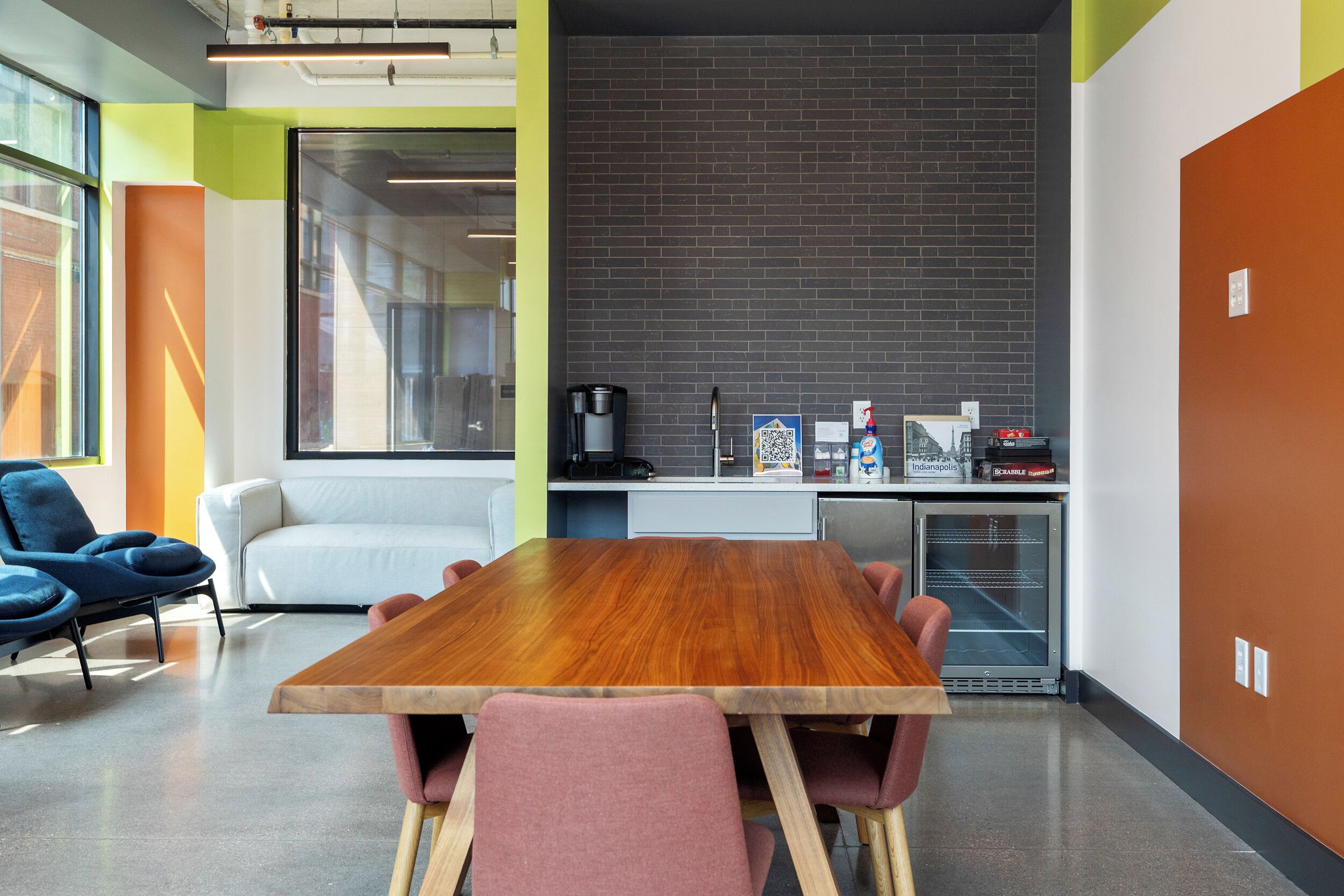 Uma sala de reuniões moderna com mesa de madeira, cadeiras cor-de-rosa, sofá branco e parede de tijolos.