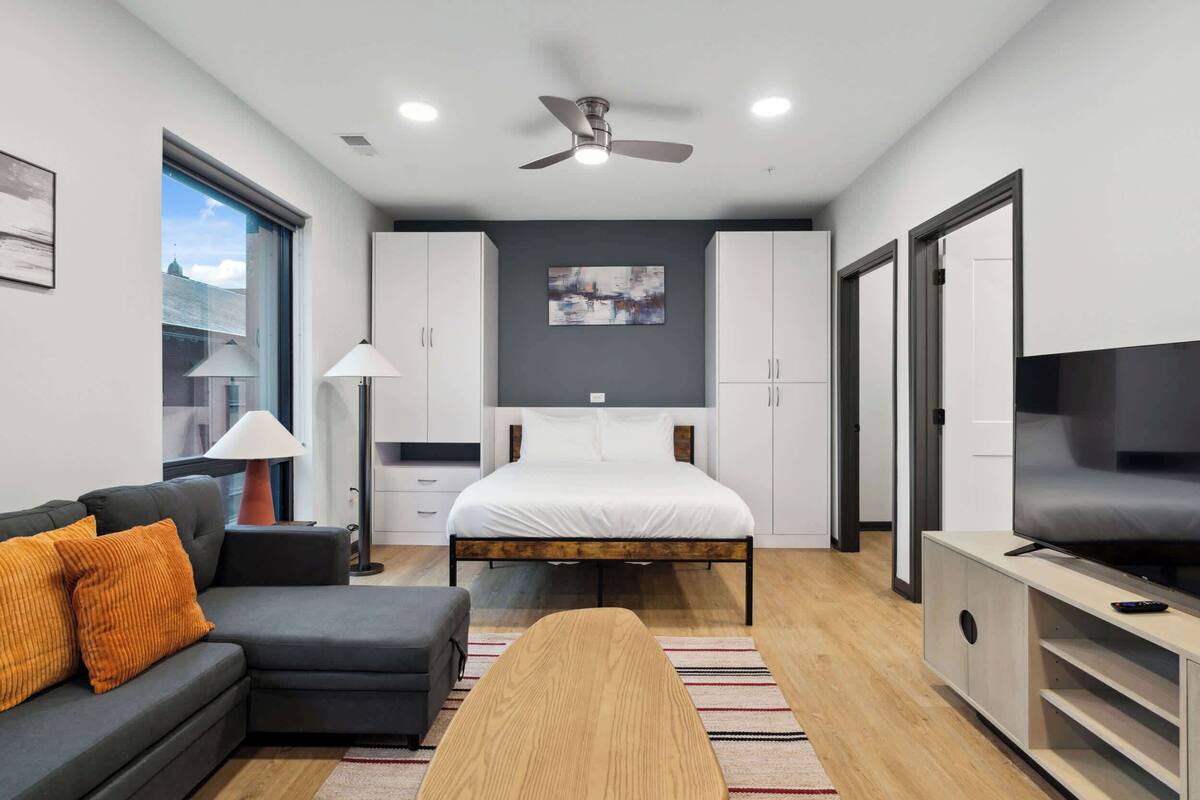 A modern bedroom with a bed, a sofa, a TV, and a ceiling fan.